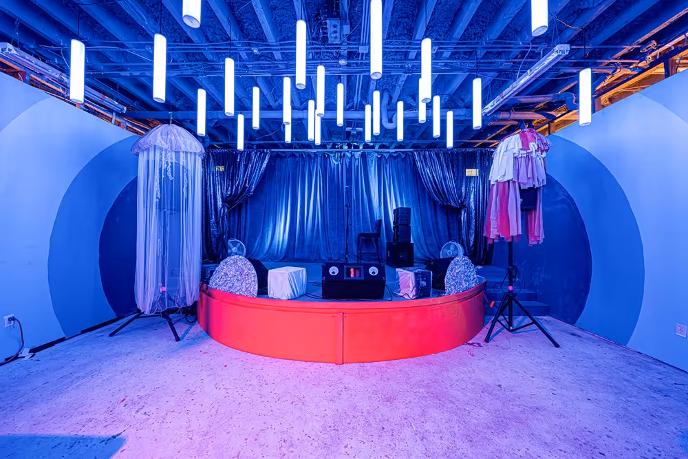 Stage setup at The Supermarket Atlanta featuring suspended LED tube lights, a circular platform, and artistic decor, creating a visually striking environment for performances and events.