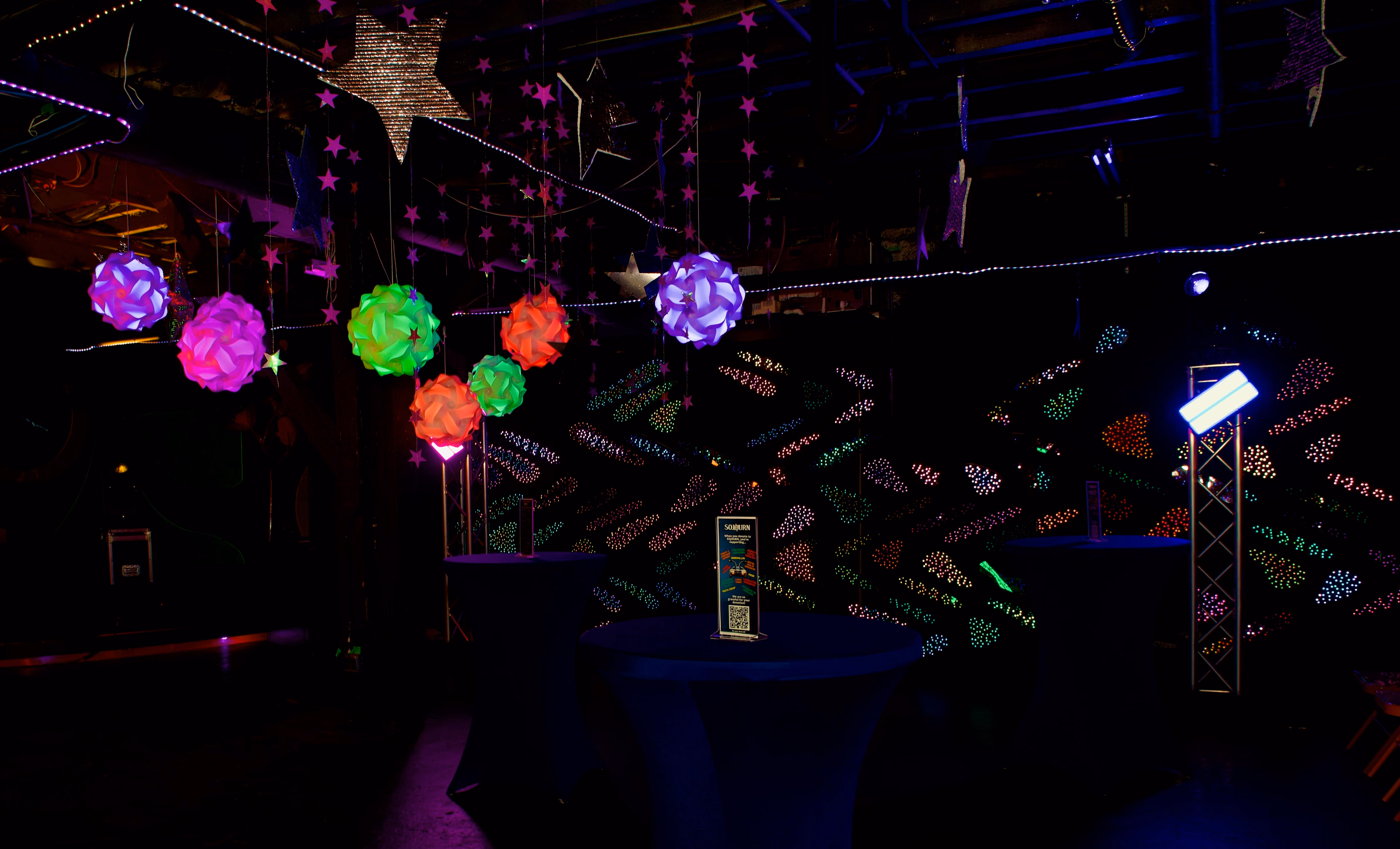 Colorful spherical lights hanging above dark tables with illuminated star decorations in the background.