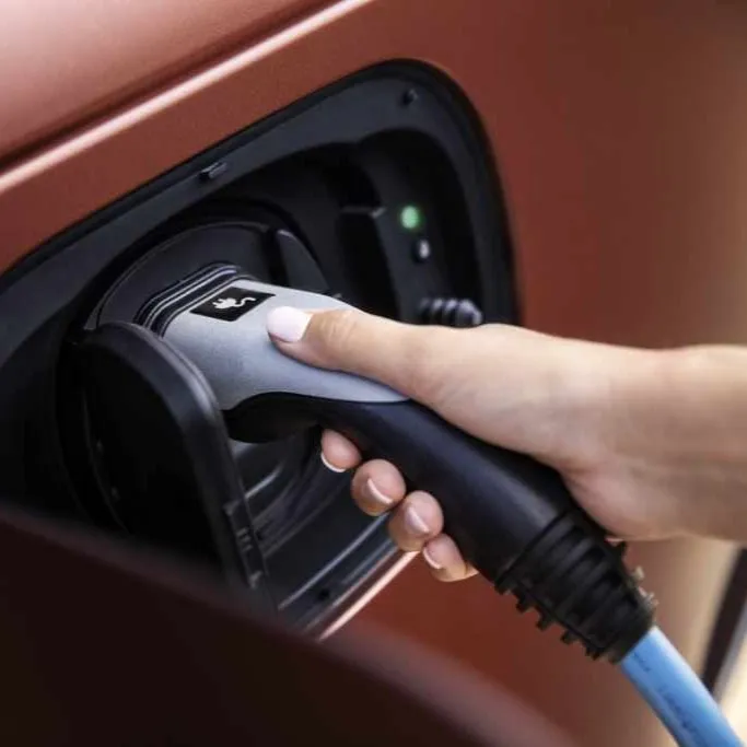 A hand plugging an electric vehicle charging connector into a car's charging port.