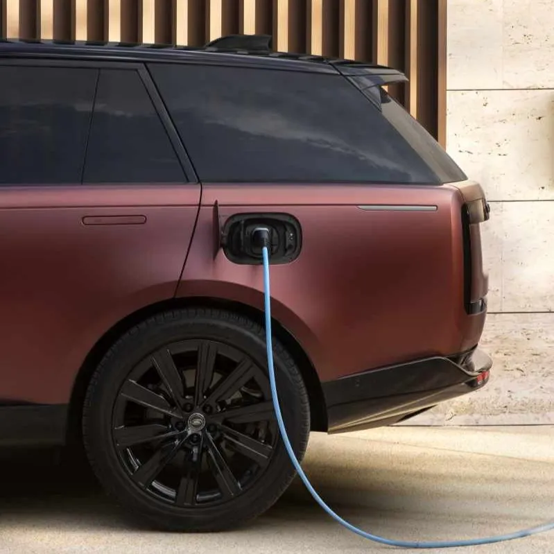 Rear side of a matte brown electric SUV plugged into a charging station with a blue cable.