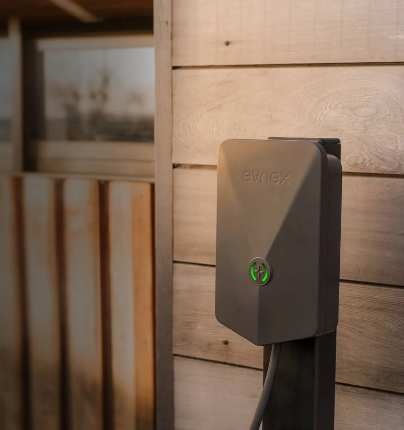 Evnex electric vehicle charging station mounted on a wooden exterior wall with a green illuminated button.