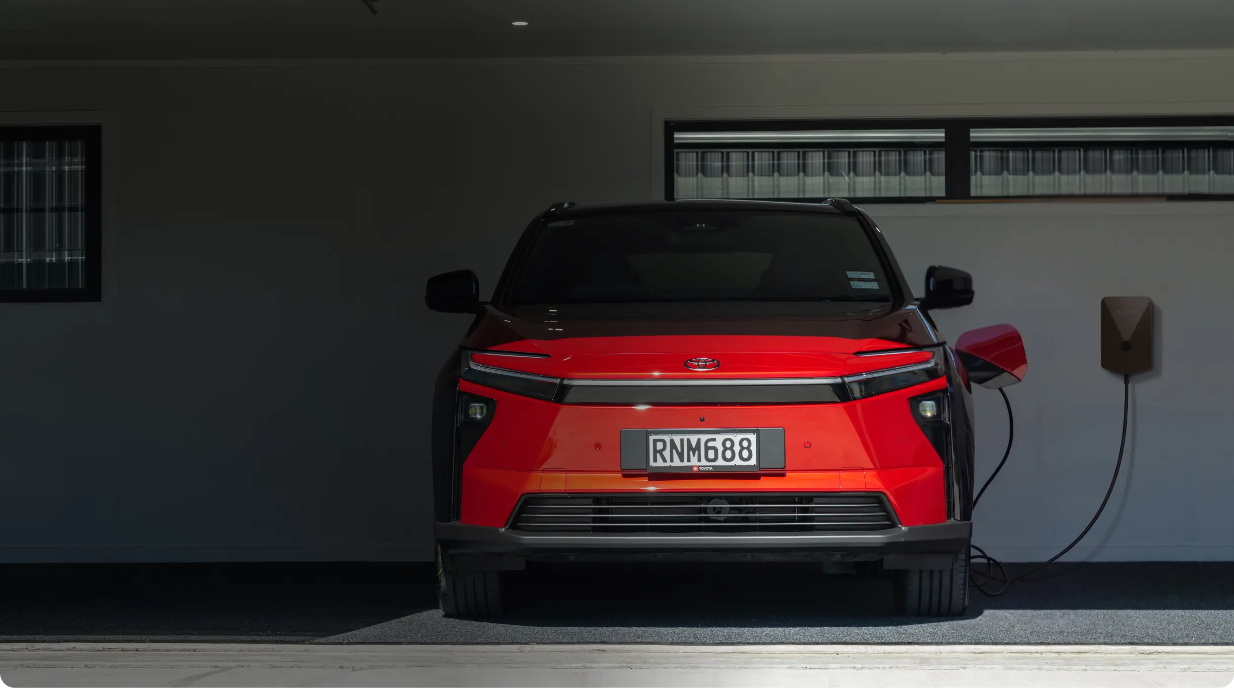 A red toyota SUV in a garage, charging with an Evnex EV charger