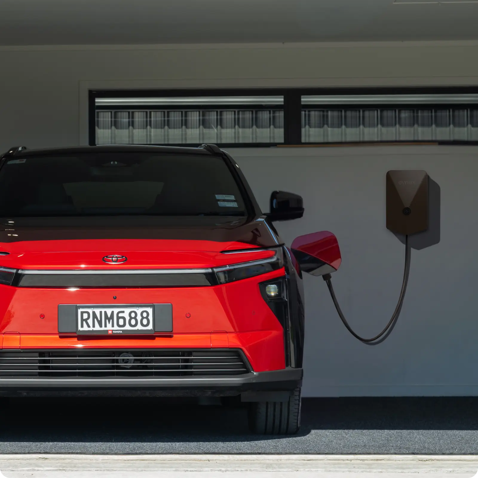 A red toyota SUV in a garage, charging with an Evnex EV charger