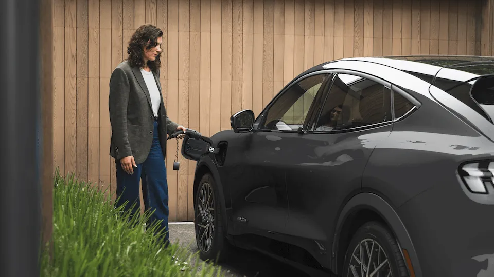 A woman plugs an EV charging cable into a car