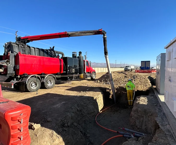 A red truck parked of Pacific West Construction next to a construction site, with workers in hard hats and machinery in the background.