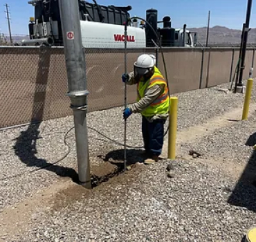 A worker of Pacific West Construction using a pipe to dig a hole in the ground.