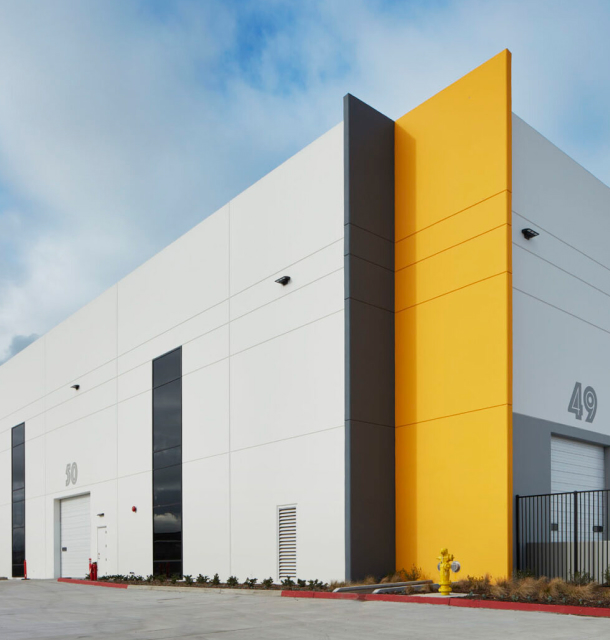 A white and yellow building with a parking lot in front, under a clear blue sky.