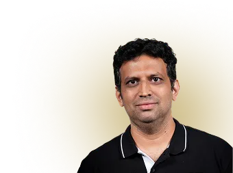 Man with short curly hair wearing a black polo shirt against a brown background.