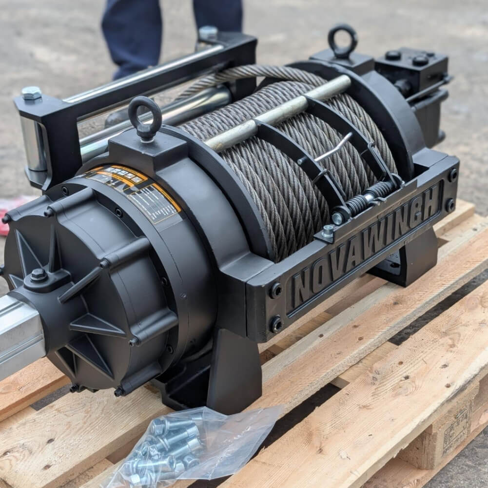 A robust black Novawinch brand hydraulic winch featuring a neatly spooled steel cable, resting on a wooden shipping pallet