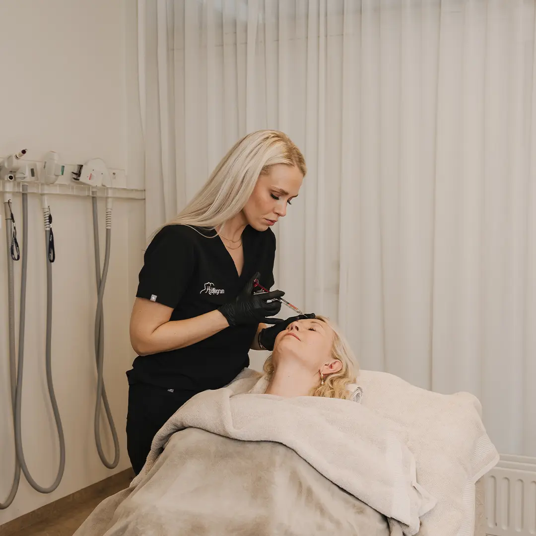 Skjólstæðingur fær hyaluronic acid booster-meðferð á enni framkvæmd af fagmenntuðum hjúkrunarfræðingi hjá Hudfegrun. Myndin sýnir meðferð í framkvæmd í björtu og nútímalegu umhverfi, þar sem háþróuð tækni kliníkurinnar sést í bakgrunni og undirstrikar fjölbreytt úrval húðmeðferða.