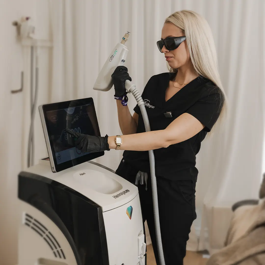 Hjúkrunarfræðingur stillir háþróaða leysitækni fyrir laserlyftingu á andliti og hálsi í einu af meðferðarherbergjum Hudfegrun. Myndin sýnir nákvæma meðhöndlun tækjabúnaðar til að tryggja örugga og sérsniðna meðferð.