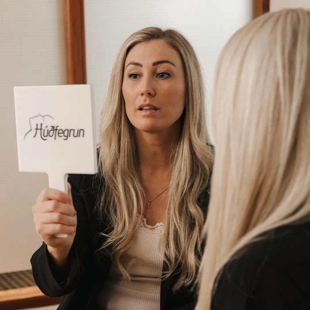 Ráðgjöf fyrir Toxín meðferð hjá Húðfegrun þar sem sérfræðingur sýnir viðskiptavini andlitssvæði í spegli og útskýrir hvernig meðferð getur minnkað fíne línur og hrukkur og gefið húðinni sléttara og ferskara yfirbragð.