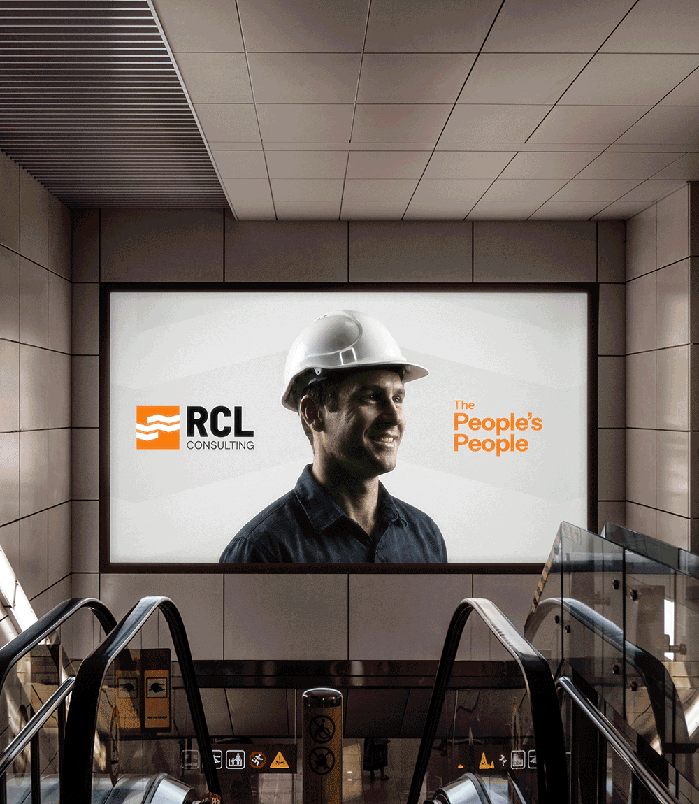 Billboard in a subway station showing a smiling man in a white hard hat with the RCL Consulting logo and the phrase 'The People's People.'