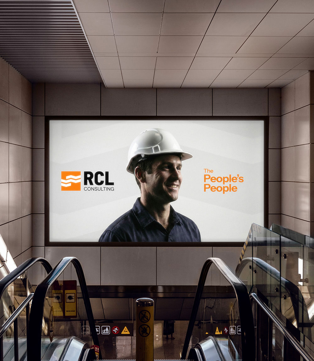 Billboard in subway station showing a smiling man in a white hard hat with the text 'RCL Consulting' and 'The People's People'.