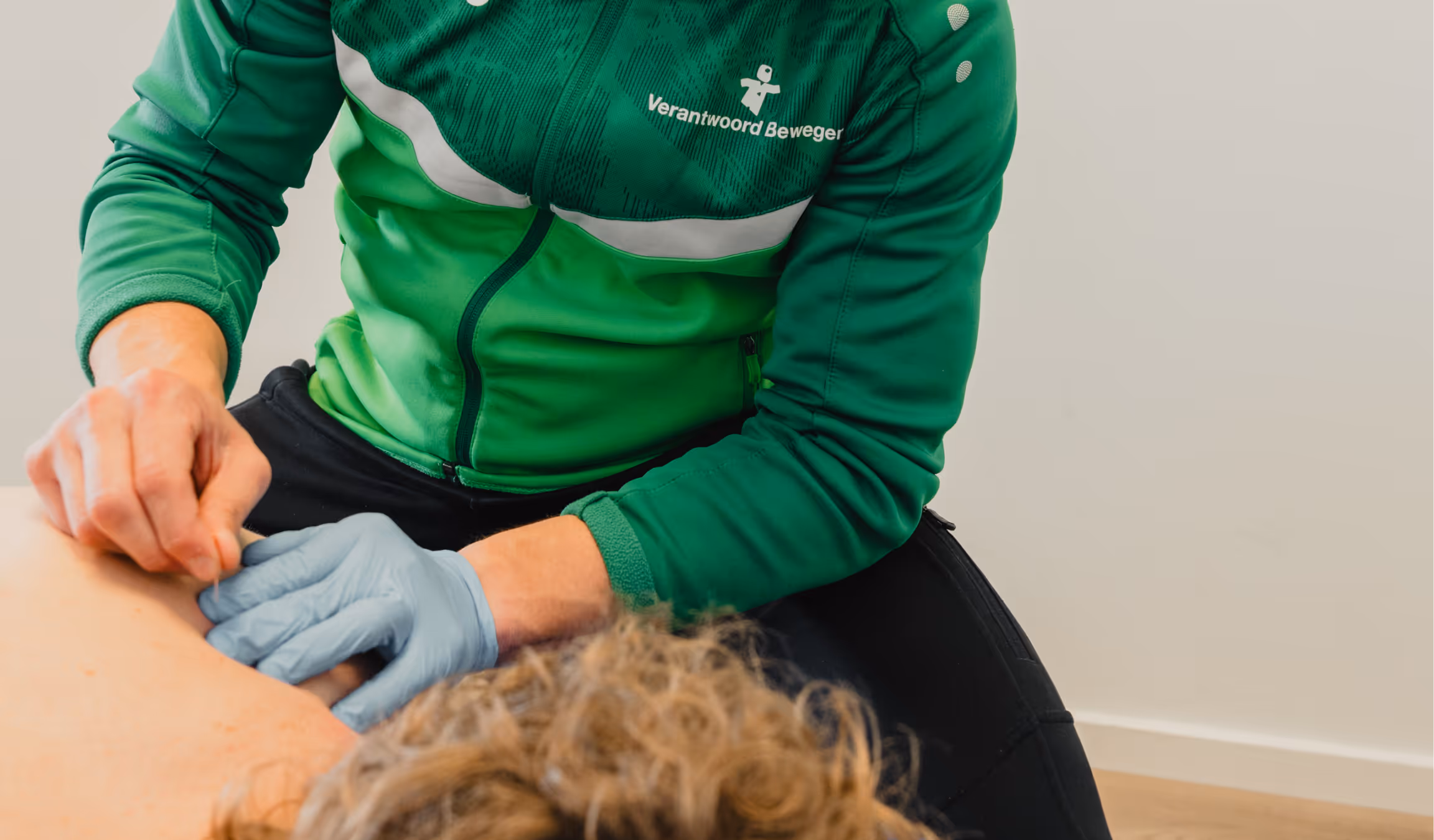 Therapist wearing green jacket performing dry needling on a patient's back.