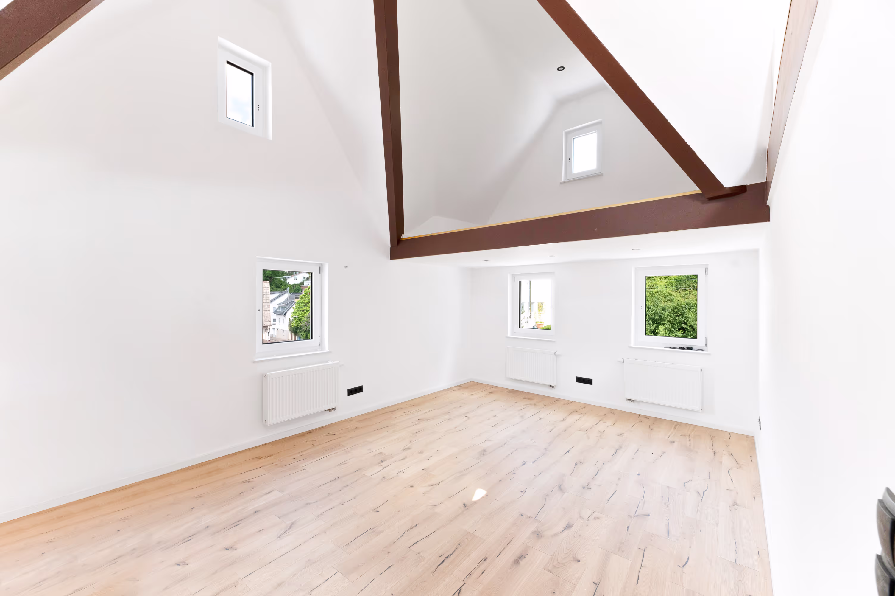 Bright, spacious living room with wooden flooring, high ceilings, exposed wooden beams, and multiple windows providing natural light.