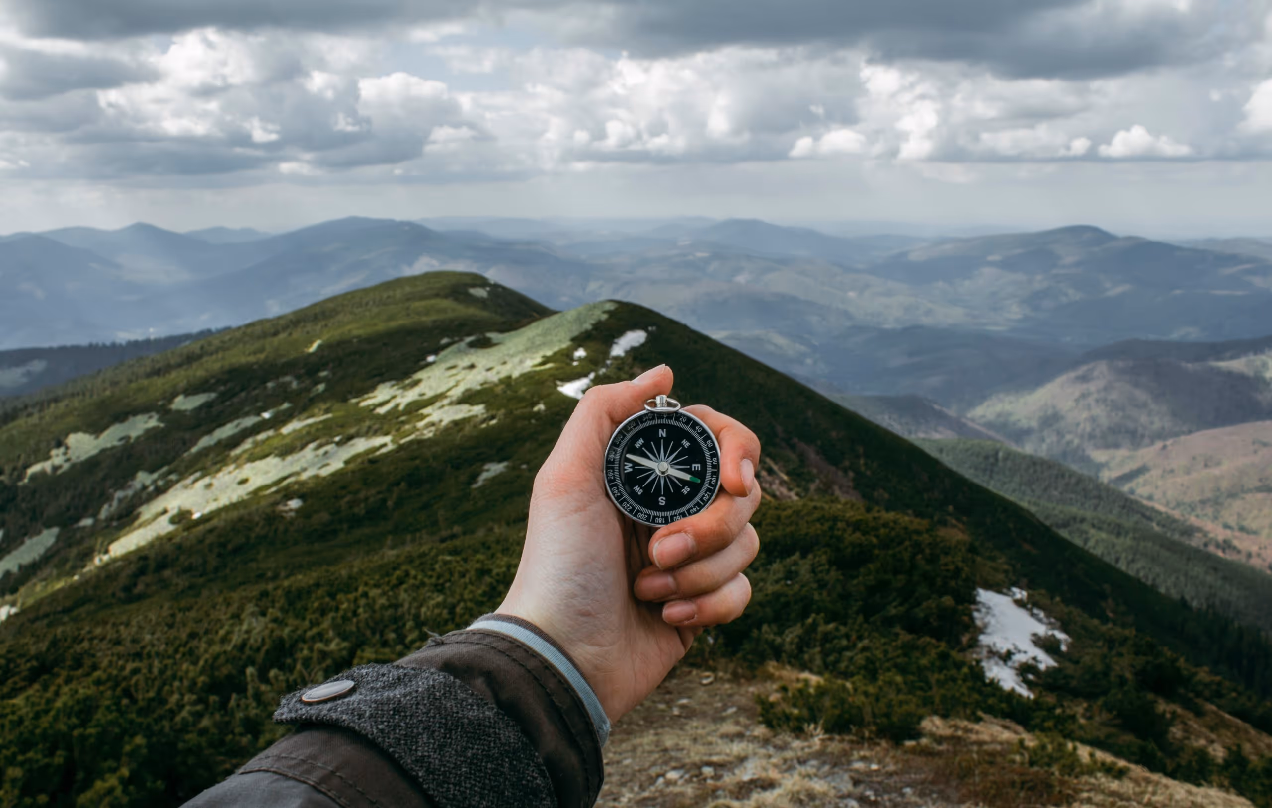 Hand holding a compass with green mountains in background