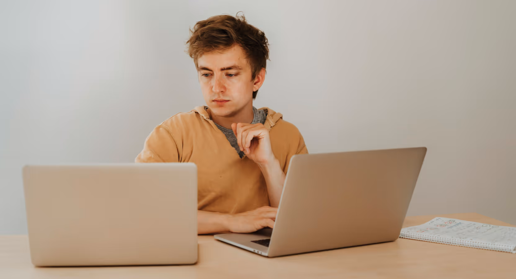 A man sits at a table with two laptops, focused on his work in a healthcare setting.