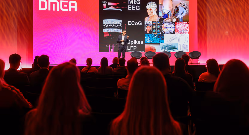 Speaker presenting neurotechnology and brain imaging tools on stage at DMEA Berlin 2025 with an audience watching attentively.