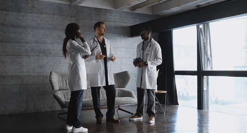 Three healthcare professionals in lab coats discussing privacy protocols in a modern clinic setting.