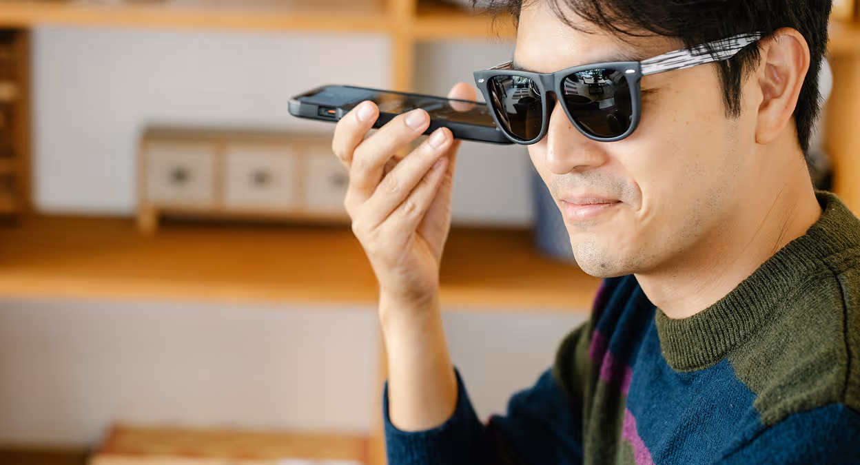 Man sitting by a window, speaking into his smartphone using a voice assistant, representing hands-free digital interaction.