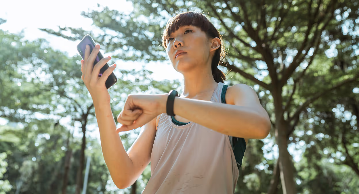 Woman in sportswear interacting with her smartphone and smartwatch using voice commands in an outdoor setting.