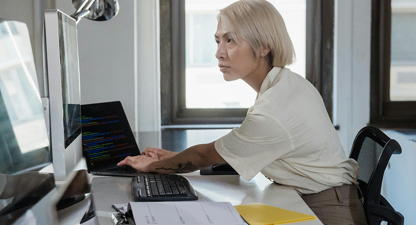 Engineer reviews code on a laptop and external monitor in a modern office, validating AI-generated changes before deployment.