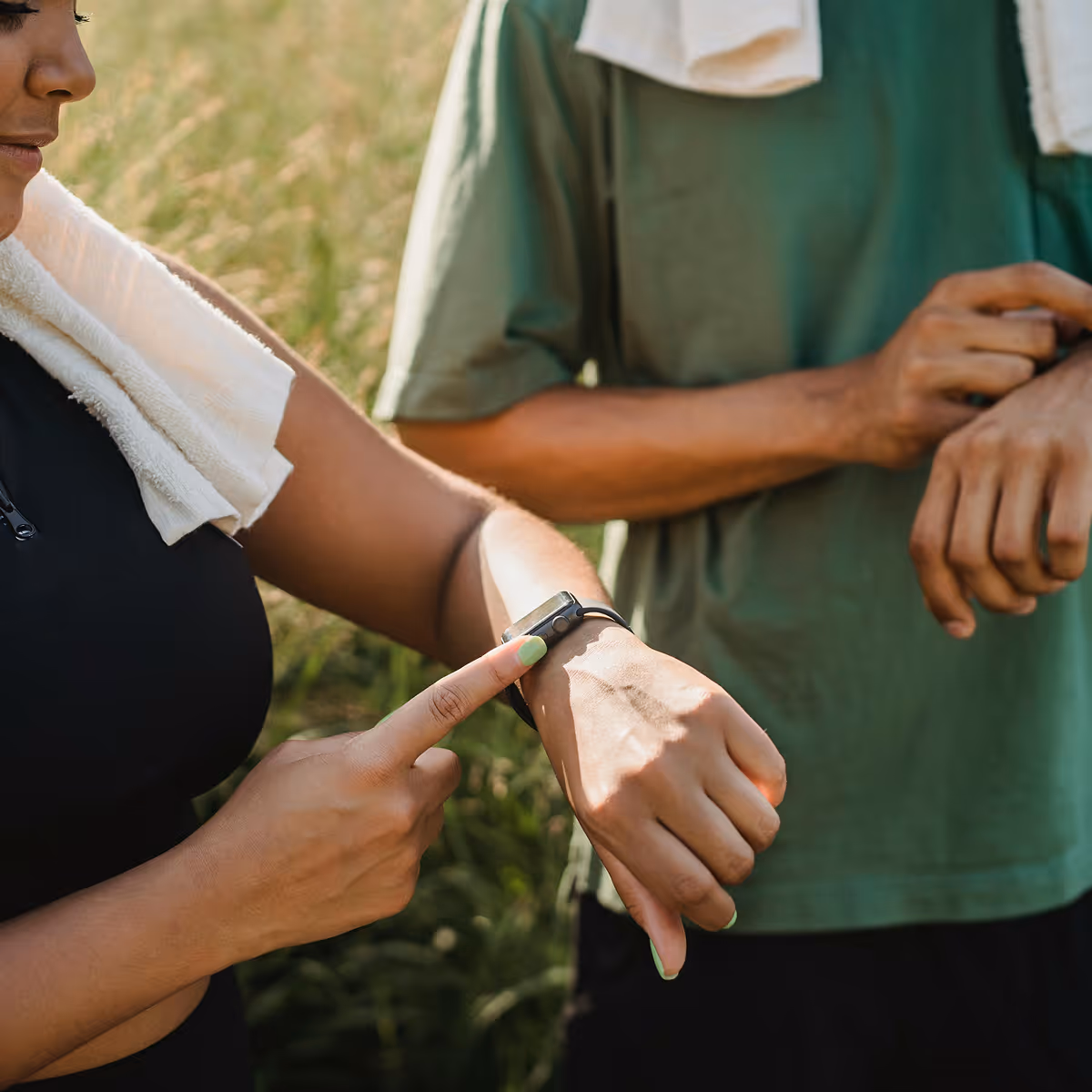 A man and woman stand in a field, each wearing a smartwatch, engaged in a discussion about health and fitness data.