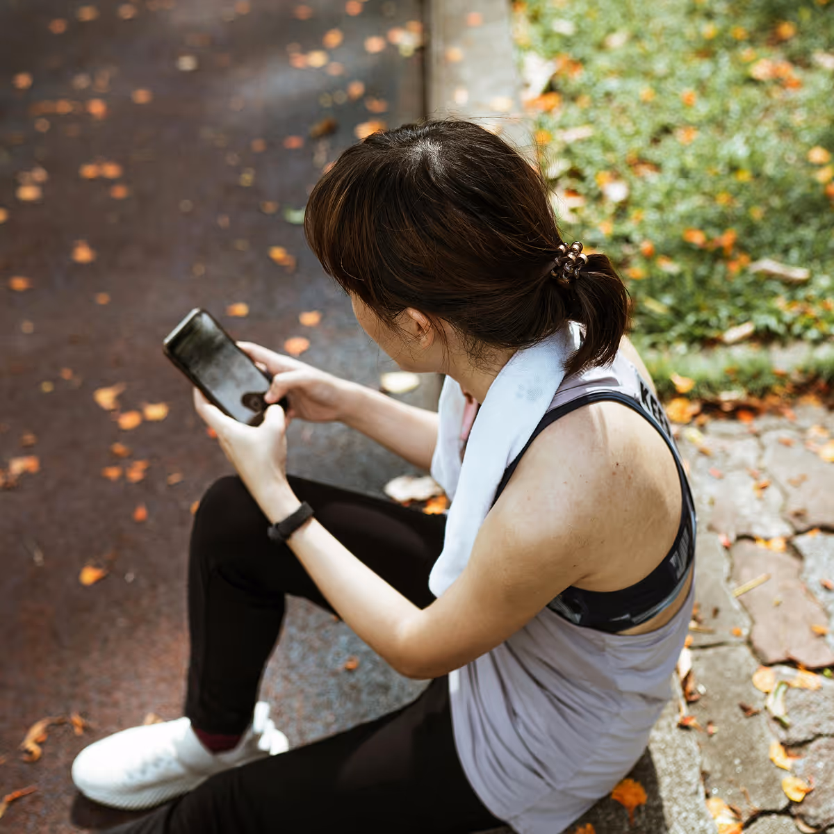 A woman sitting on the ground, focused on her phone, amidst a vibrant outdoor setting.