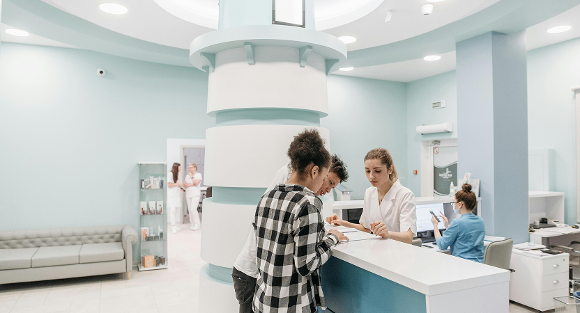 Modern healthcare facility reception area with medical staff assisting patient at front desk