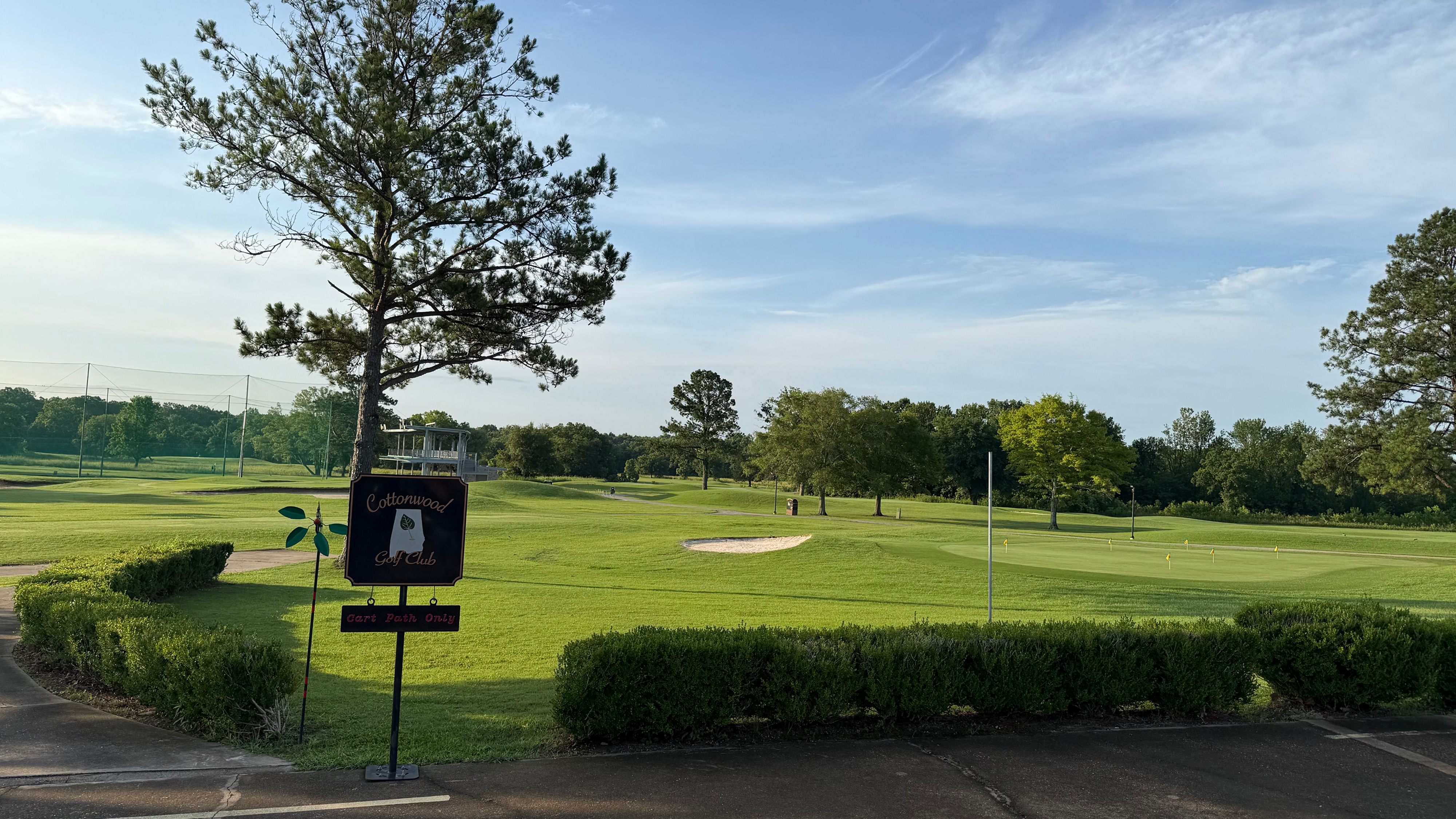 Wide view of a golf course with two golf carts parked on a paved area under a clear blue sky.