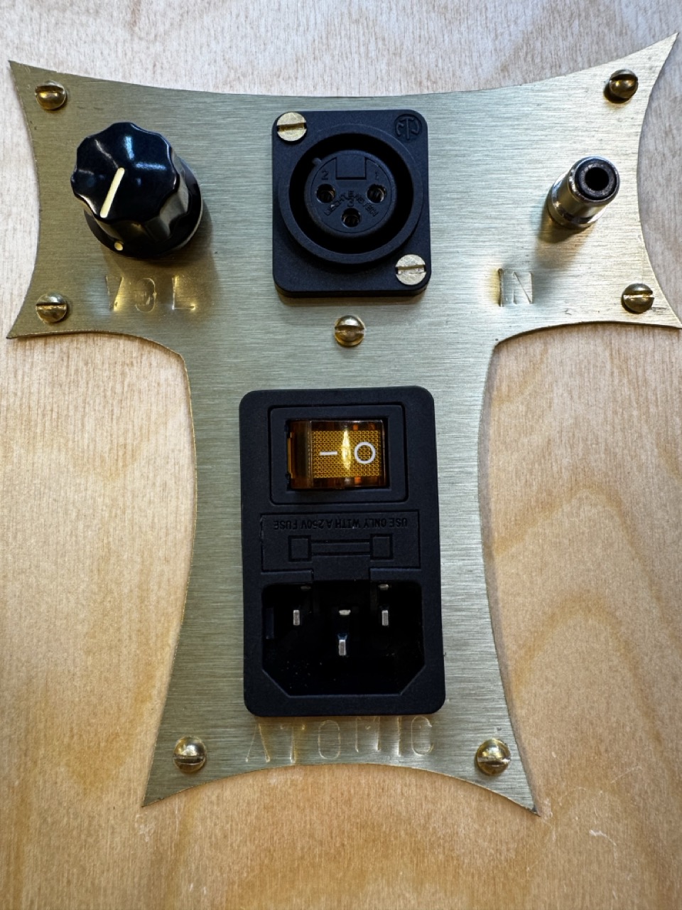Closeup of custom tiki "T" brass control plate on rear of Atomic Bookshelf Monitor handmade by Desmond Bowe of Tiki Tube Amps showing power switch, volume control, and line inputs.