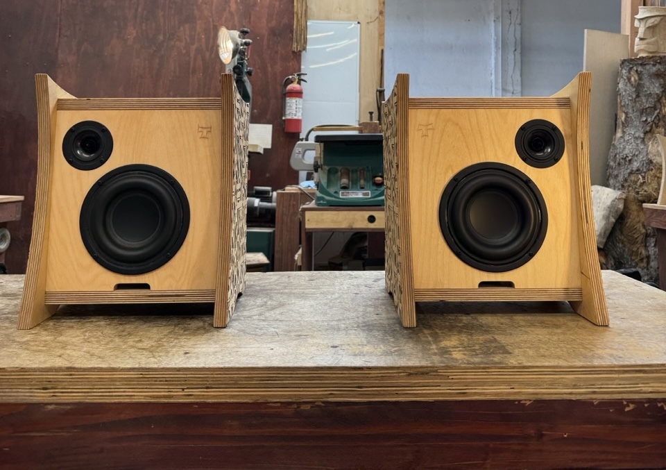 Front view of Atomic Bookshelf Monitors custom built by Tiki Tube Amps for DJ The Gaslamp Killer showing front drivers, carved tiki "T" logo, and front vented port on display in the Tiki Tube Amps Los Angeles workshop