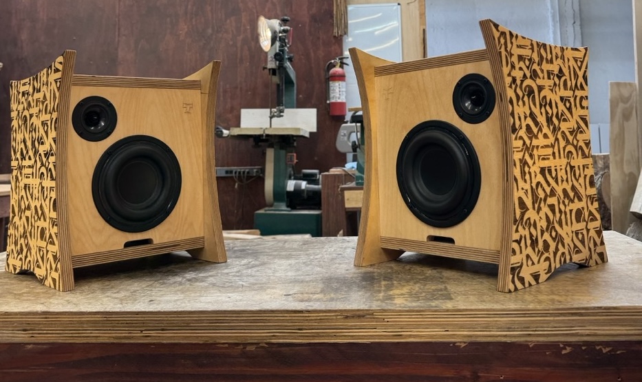Front view of Atomic Bookshelf Monitors custom built by Tiki Tube Amps for DJ The Gaslamp Killer showing front drivers, carved tiki "T" logo, and custom side panels etched by Cryptik on display in the Tiki Tube Amps Los Angeles workshop