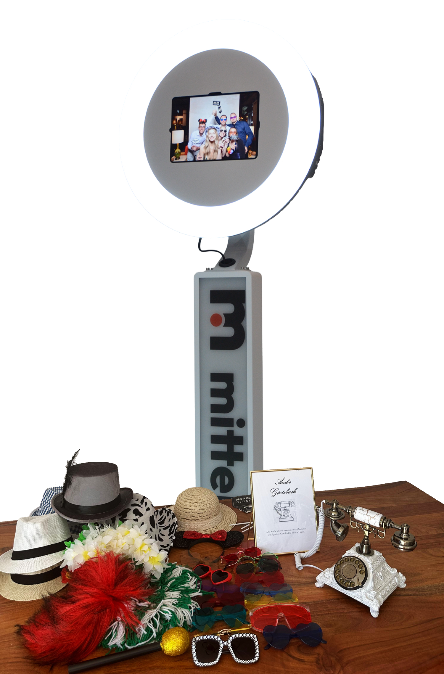 Fotobox mit Ringlicht, digitalem Display, diverse Hüte, bunte Brillen, und ein altertümliches Telefon auf einem Holztisch.
