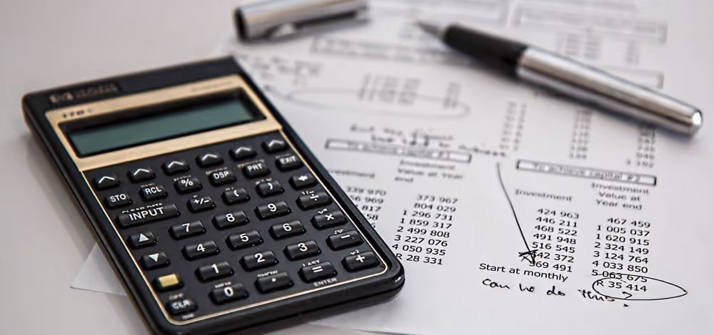 Calculadora y bolígrafo sobre documentos financieros con números y cálculos