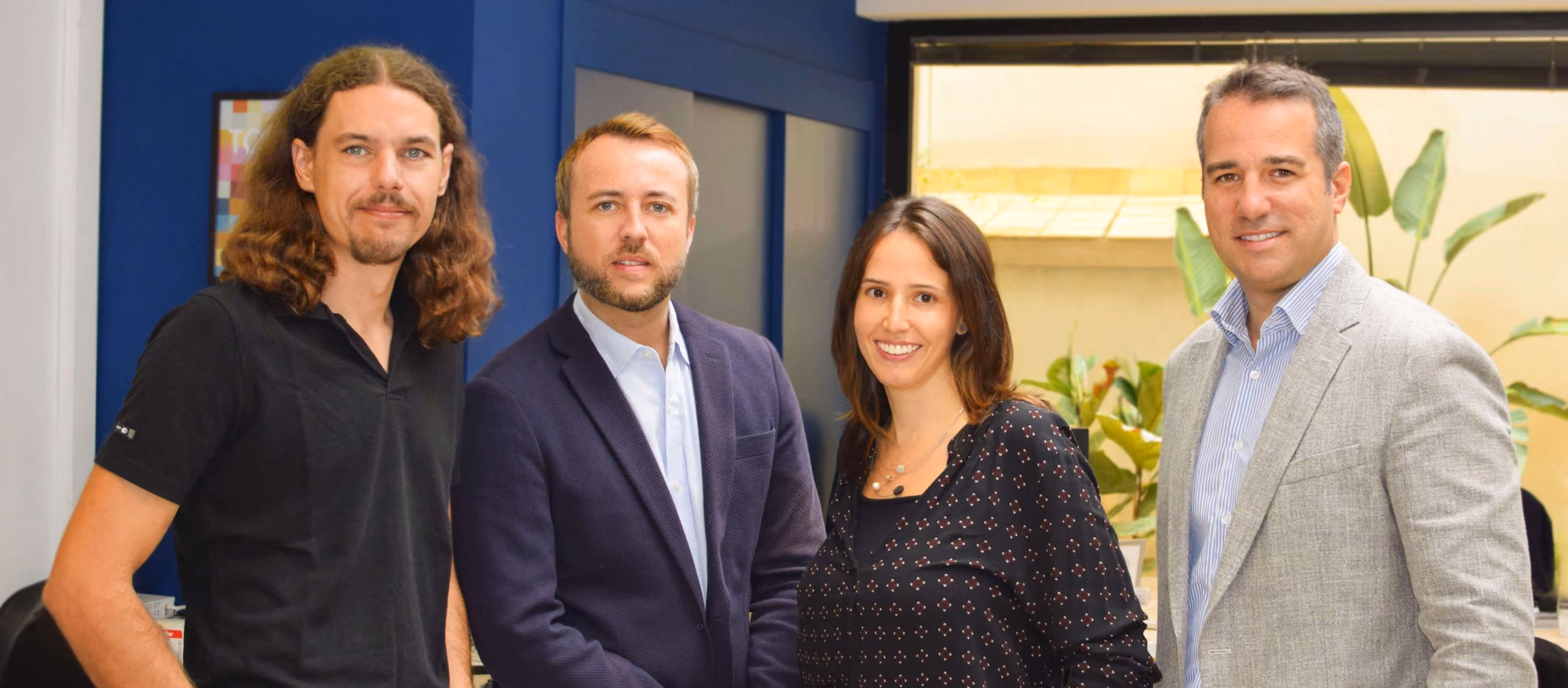 Cuatro profesionales sonrientes posando juntos en una oficina moderna