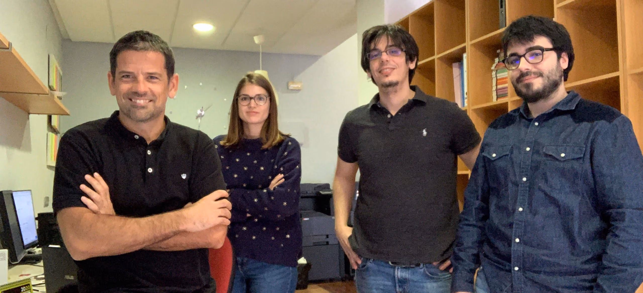 Cuatro profesionales posando juntos en una oficina con estanterías