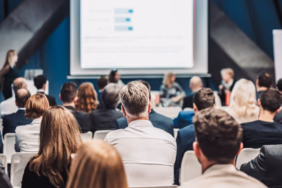 People sitting at a conference, watching a presentation on the big screen