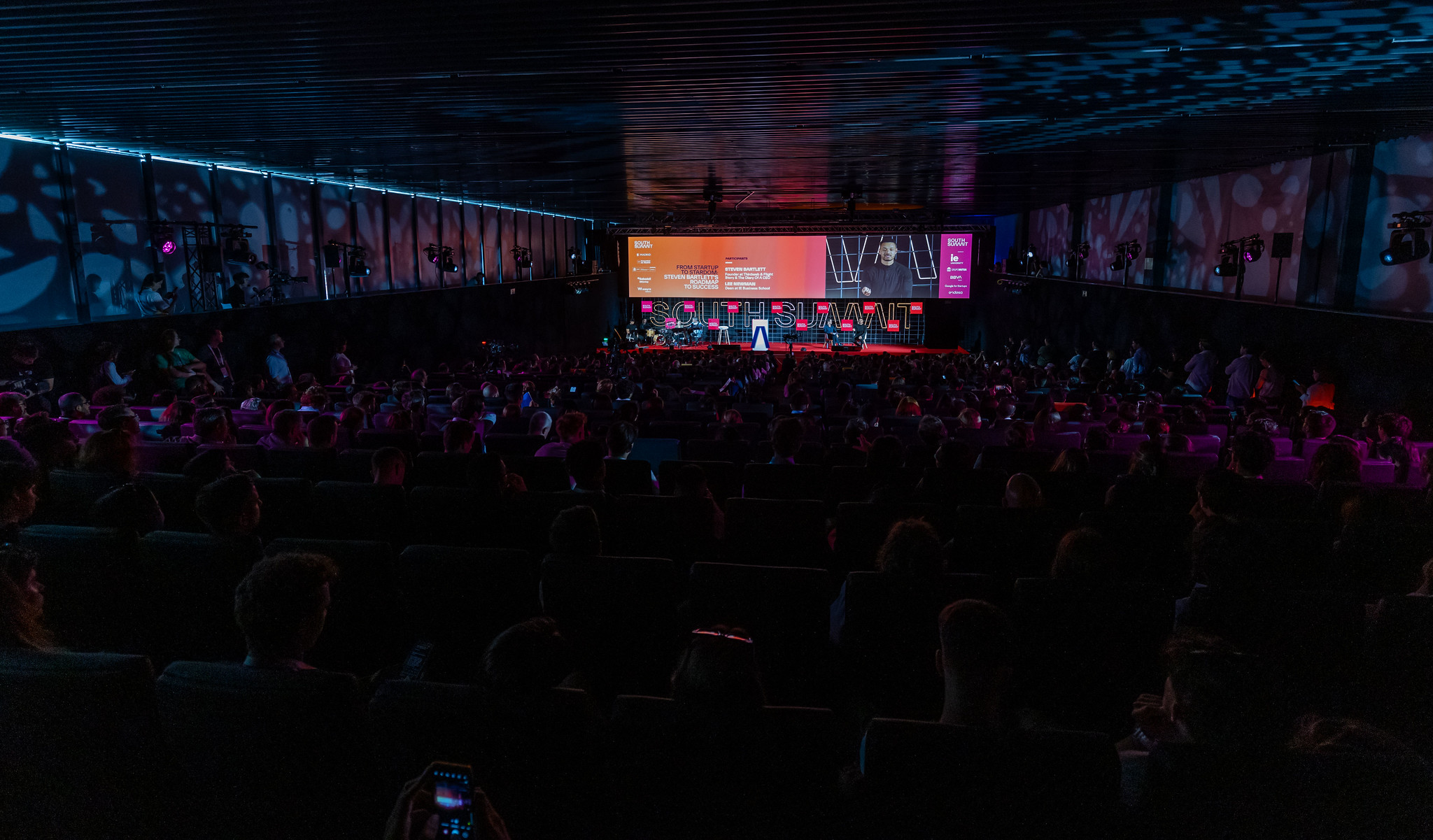 Salón oscuro lleno de gente en la conferencia South Summit con escenario iluminado
