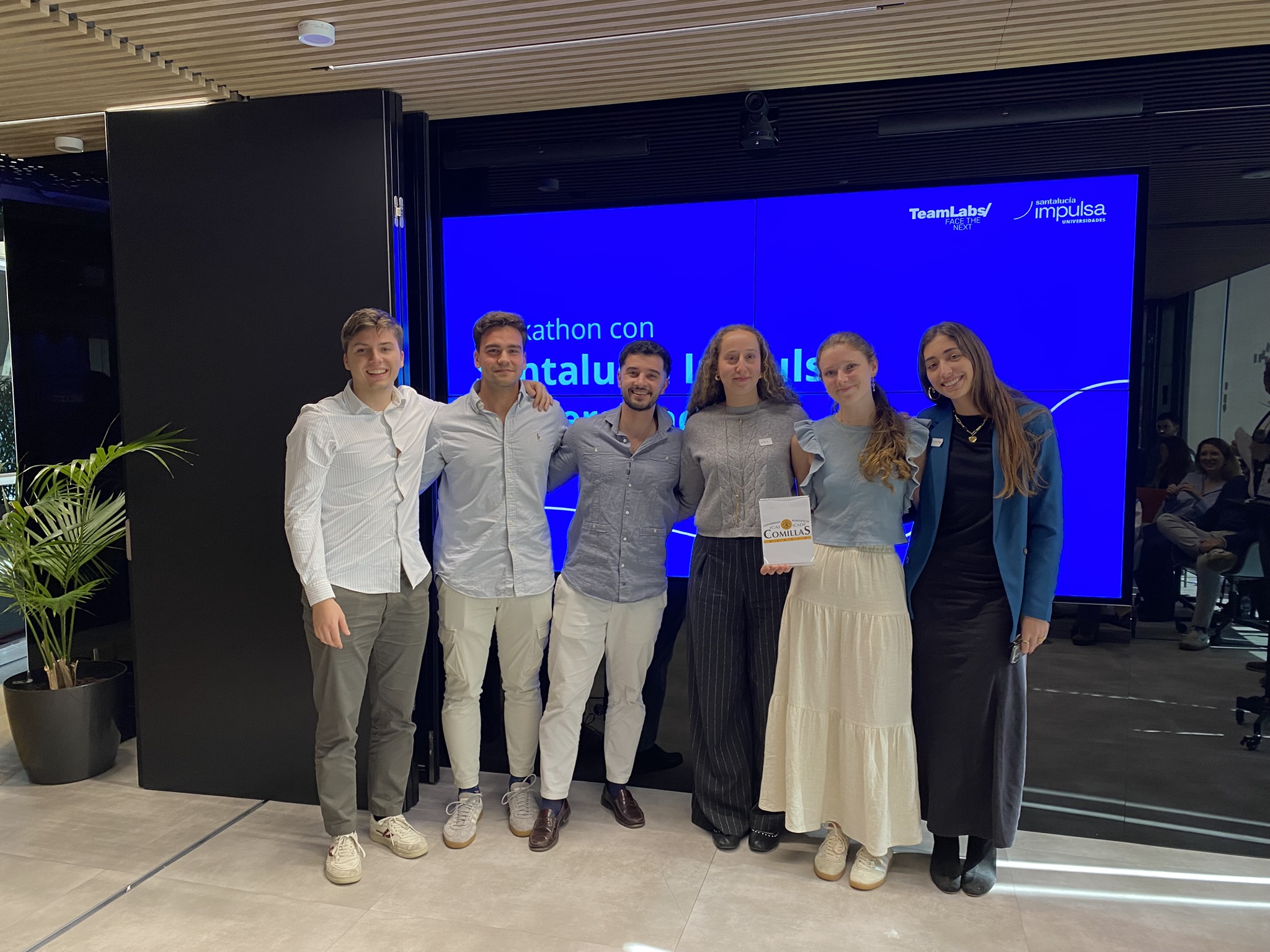 Grupo de seis personas en evento de TeamLabs con pantalla azul de fondo