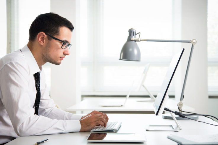 Hombre con gafas trabajando en computadora con lámpara de escritorio plateada