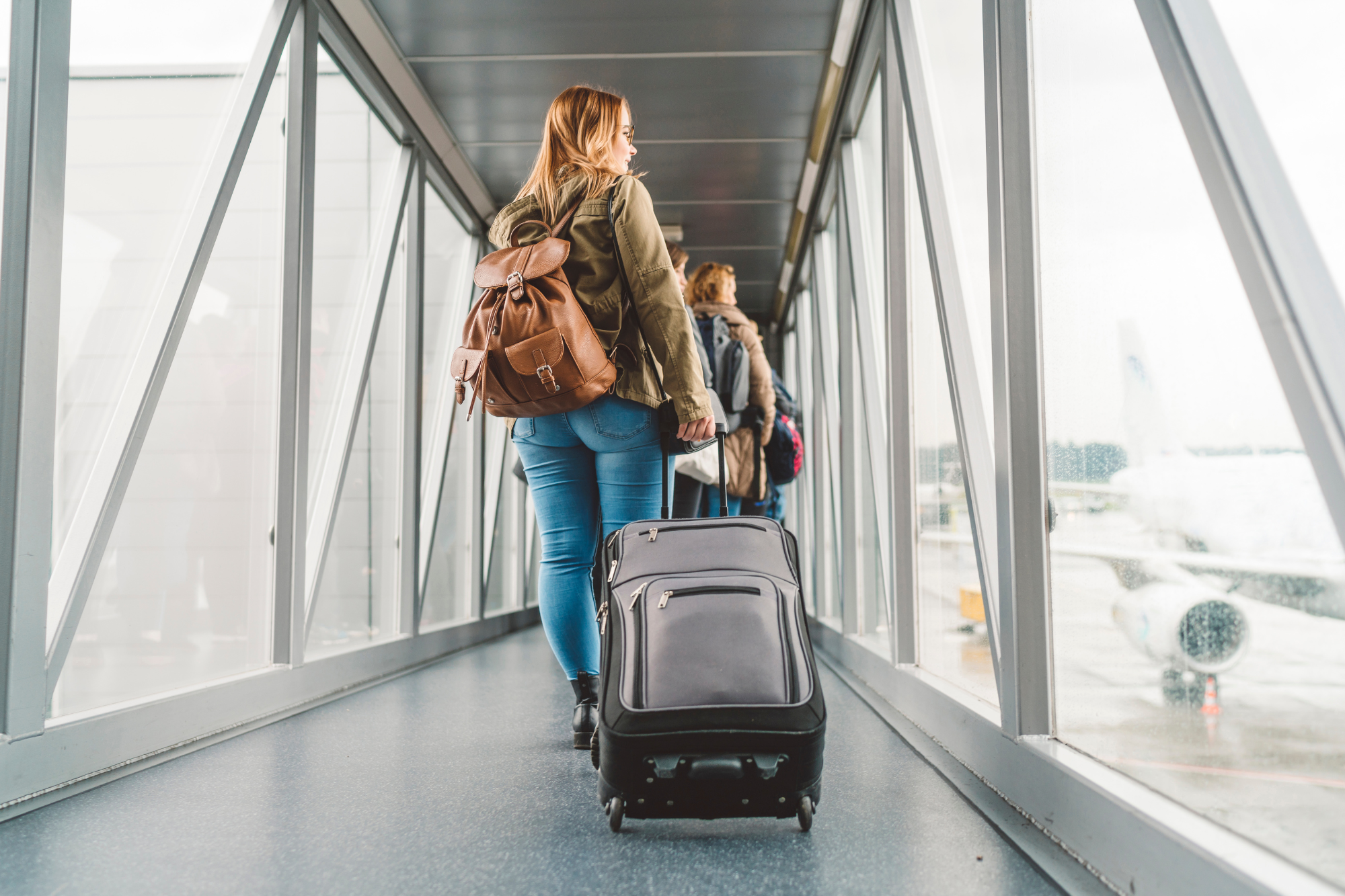 Mujer con mochila y maleta caminando por pasarela de aeropuerto