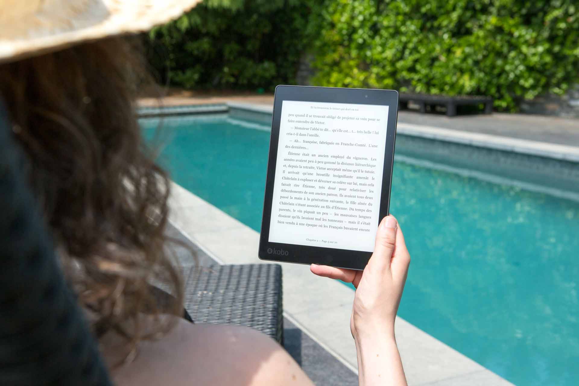 Persona leyendo una newsletter en un libro electrónico junto a una piscina durante las vacaciones de verano