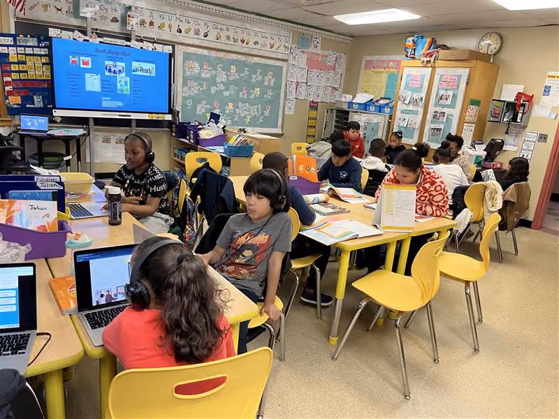 Elementary students working independently at desks with laptops and headphones