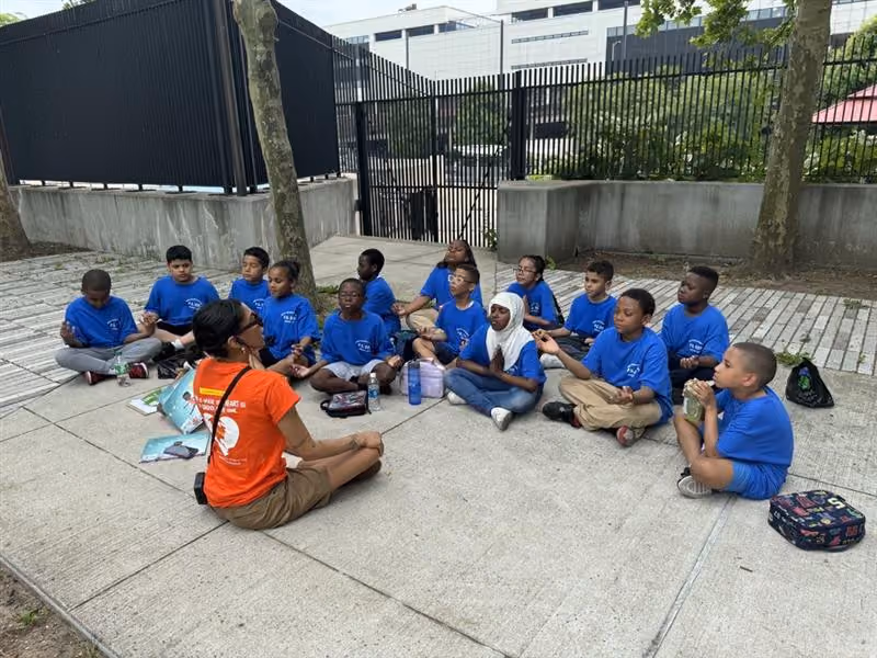 Students in blue shirts meditate outdoors with a teacher
