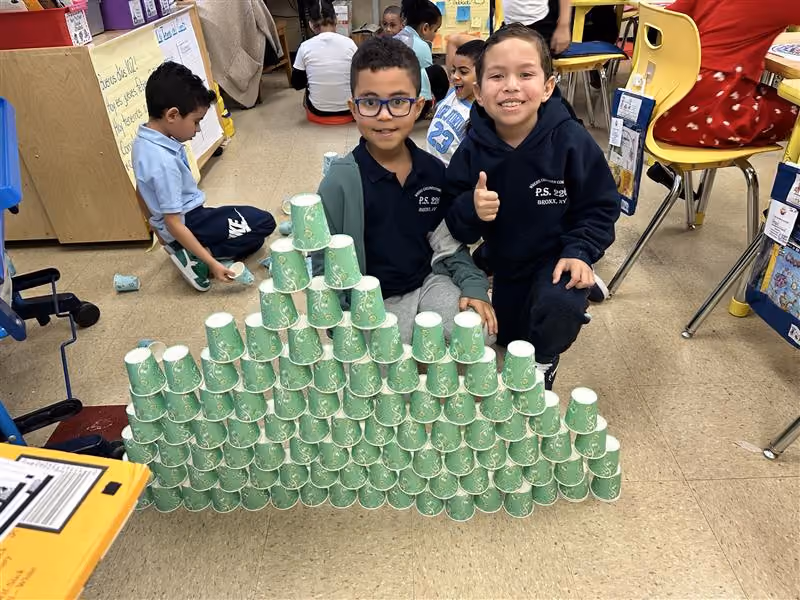 Two students proudly display their tall paper cup tower in class