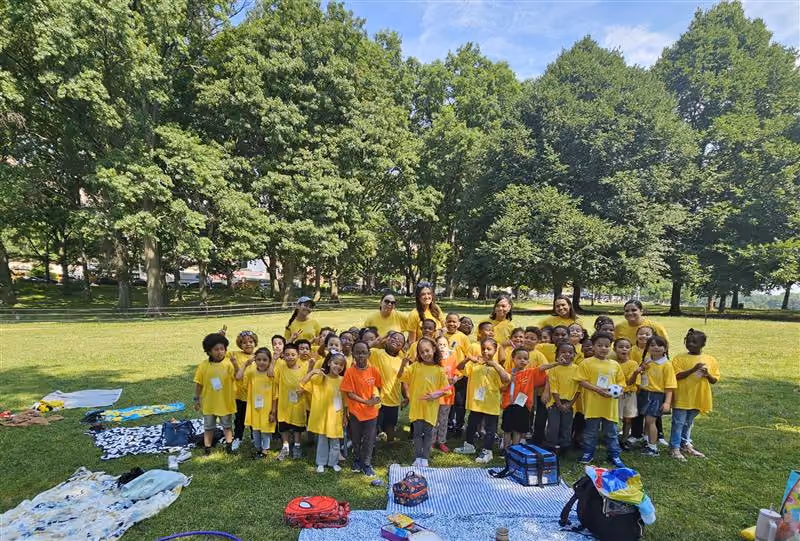 Students and teachers in yellow shirts pose outdoors at a park