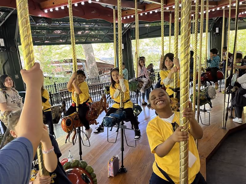 Students in yellow shirts riding a carousel on a field trip