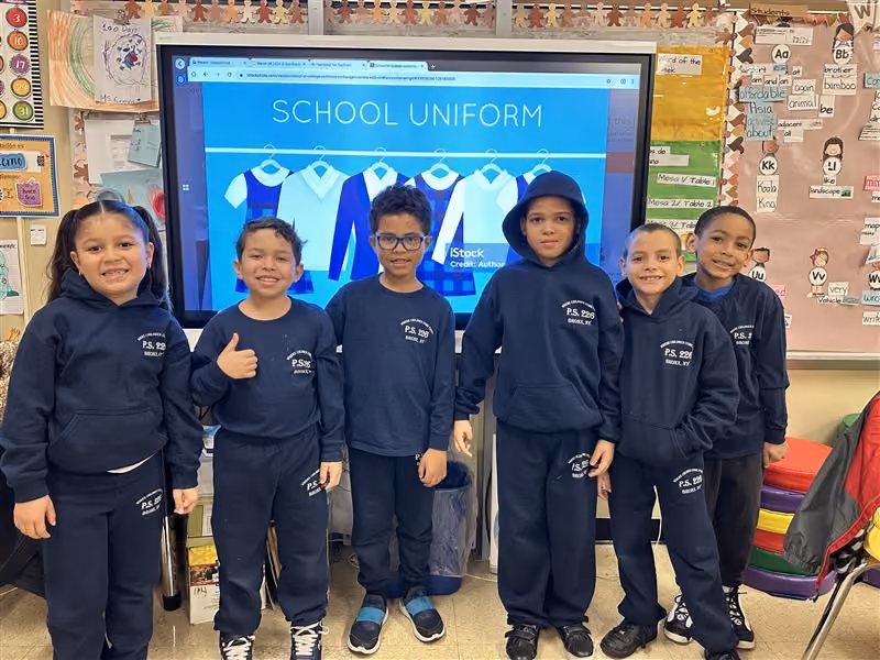 Six PS 226 students in navy uniforms pose before a smartboard